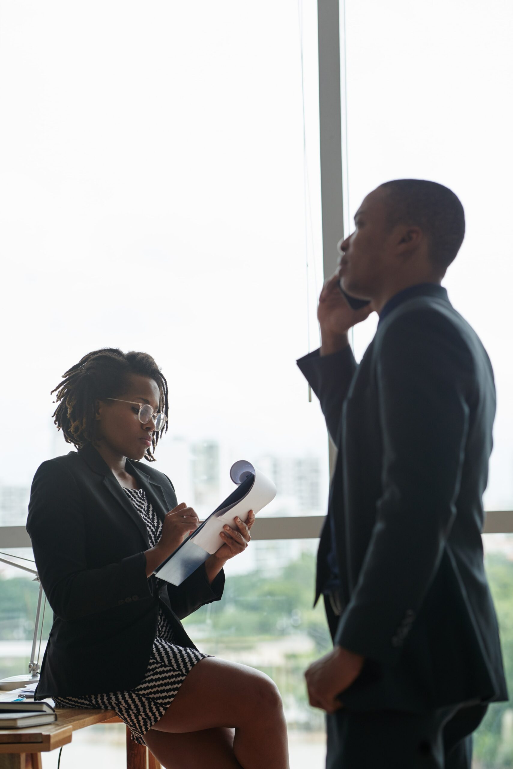 black-businessman-talking-phone-female-colleague-writing-notepad-min